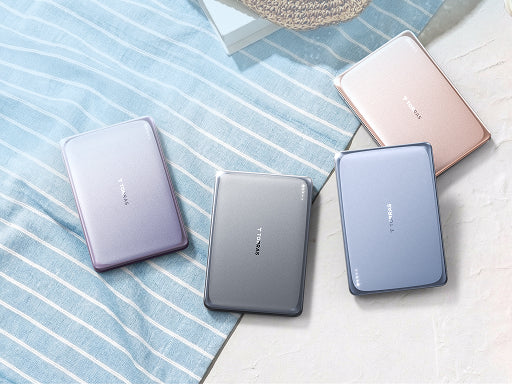 Four slim portable power banks in pastel colors arranged on fabric and a light textured surface