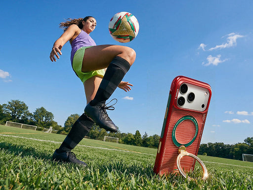 Red phone case with ring stand on a soccer field beside a player juggling a ball