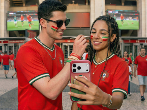Two soccer fans in red jerseys taking a selfie outside a stadium with a phone in a colorful case