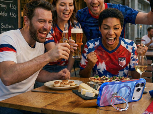 Fans celebrating at a table with food and drinks beside a phone in a blue case with ring stand