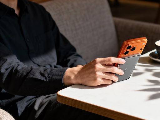 Person holding a smartphone with a TORRAS magnetic power bank attached while sitting at a cafe table