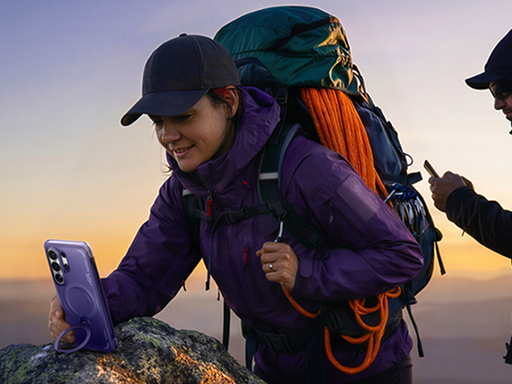 Hiker resting a purple smartphone on a rock using its built-in ring stand case while enjoying the sunset