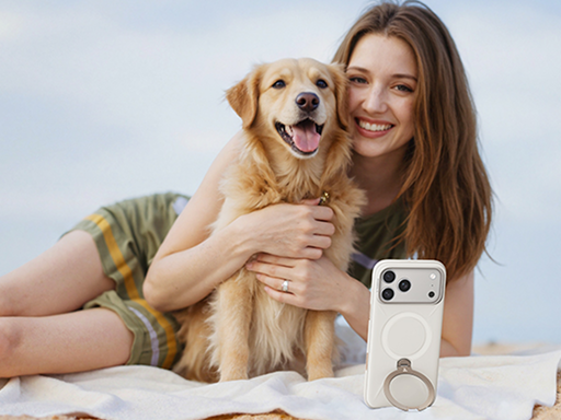 Woman hugging a golden retriever on the beach, with a white phone propped up on its ring stand in the foreground