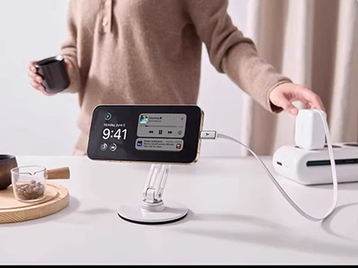 Person plugging a white charger into a power strip to charge a smartphone resting horizontally on a desk stand