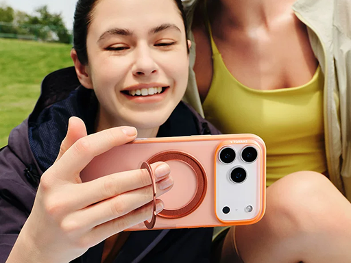 Two smiling women outdoors taking a selfie using a white and orange phone case with its ring stand pulled out