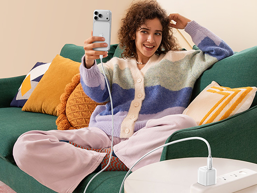Smiling woman on a green sofa taking a selfie while her phone charges via a white adapter on a side table