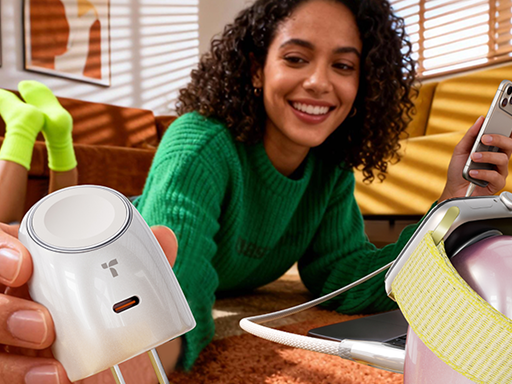 Smiling woman relaxing on the floor, holding a white charger with a smartwatch wrapped around it while using her phone