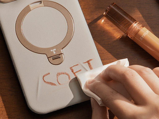 Hand wiping makeup from a beige phone case with ring stand, highlighting stain resistance and easy cleaning