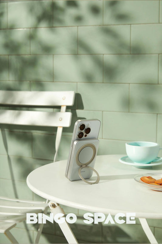 A white smartphone propped up on a café table by a magnetic power bank with a built-in ring stand.