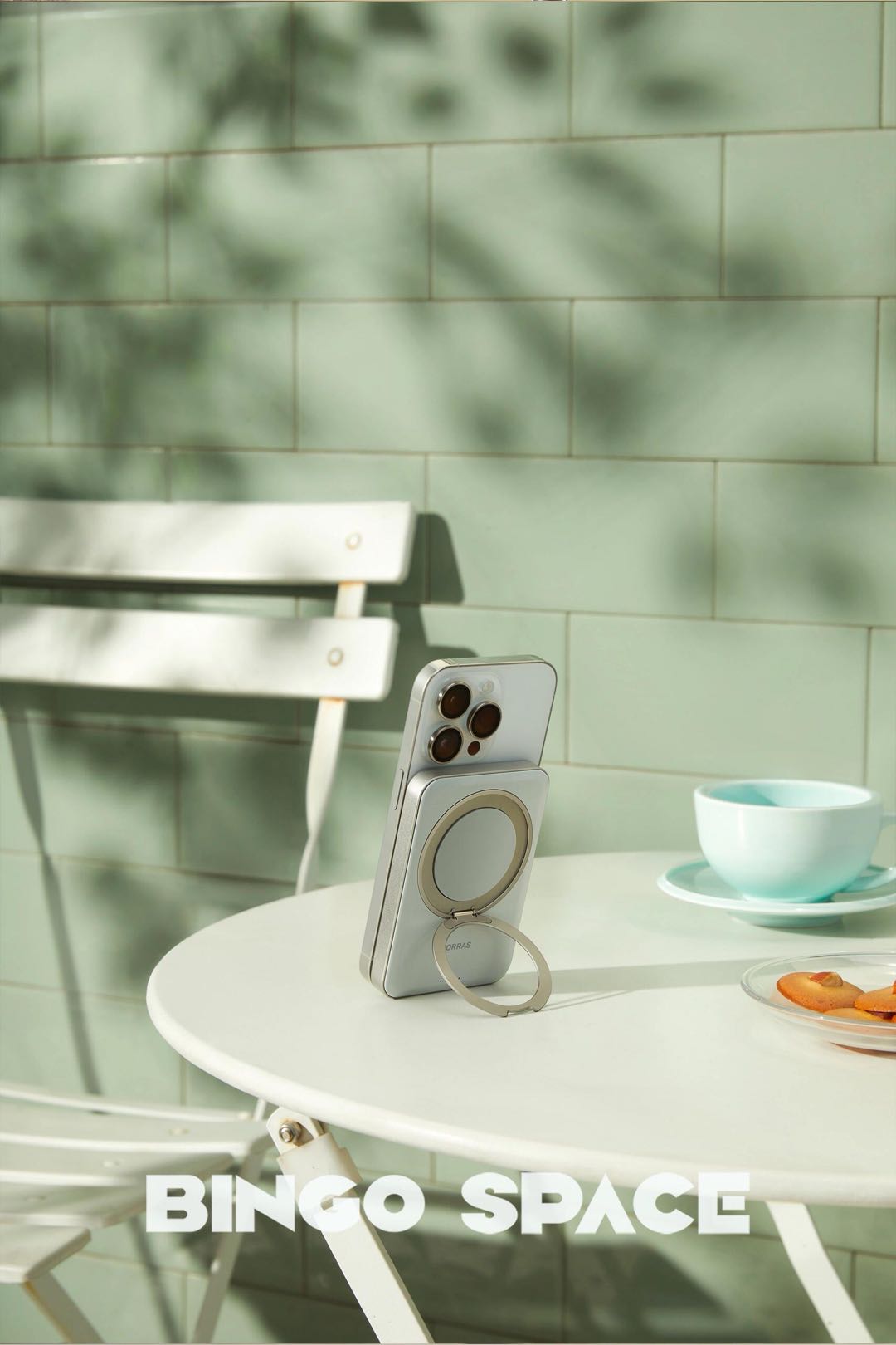 A white smartphone propped up on a café table by a magnetic power bank with a built-in ring stand.