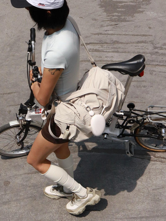 A woman carrying a beige duffle bag while walking next to a white folding bike.