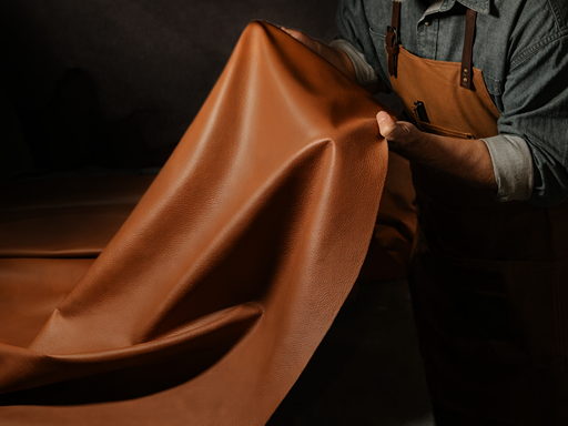 Artisan holding a large sheet of brown leather in a workshop, showcasing craftsmanship and material quality