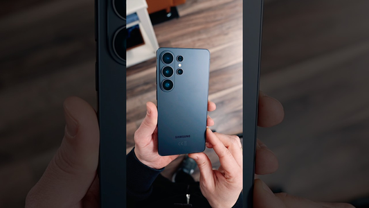 Hands holding a blue Samsung smartphone, showing rear camera module in a close-up indoor review setting
