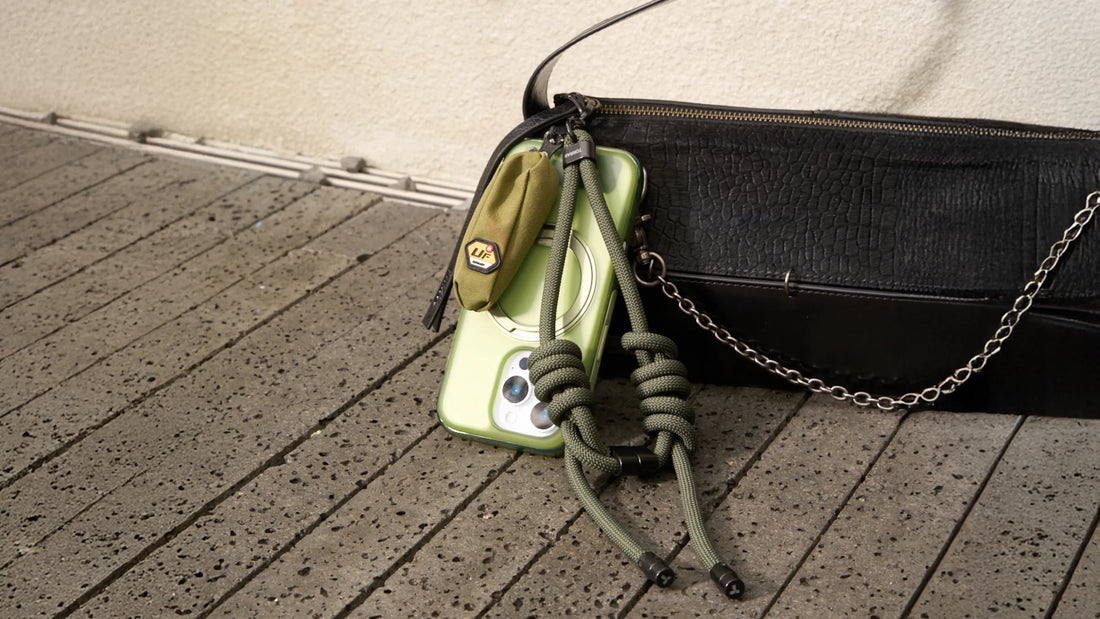 Green TORRAS phone case with crossbody lanyard placed beside a black handbag