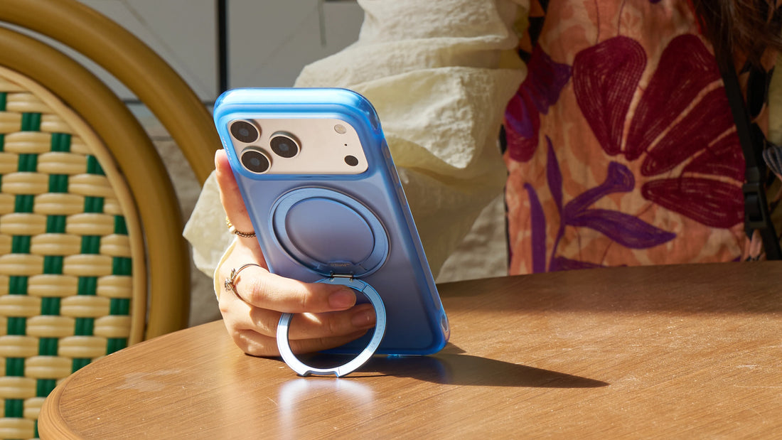 Woman holding a blue TORRAS phone case with a foldable ring stand at a sunlit café table
