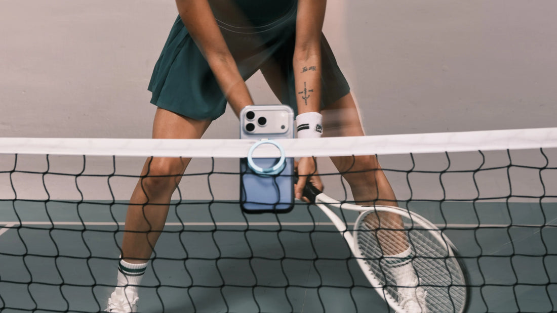 Tennis player using a blue TORRAS phone case with a foldable ring stand attached to the net