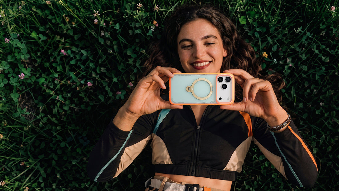 Woman lying in clover grass taking a photo with a colorful phone case and ring grip