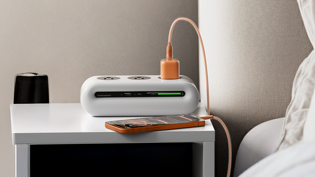 An orange phone charging next to a white power strip on a nightstand beside a bed