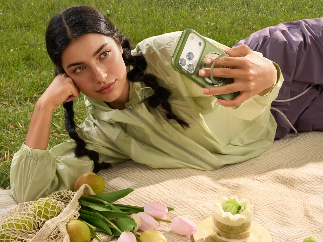Woman relaxing on a picnic blanket while holding a green phone case with a ring stand