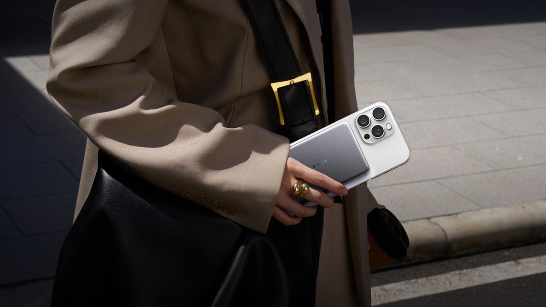 Close-up of a person holding a white iPhone with a grey Torras magnetic power bank attached to its back