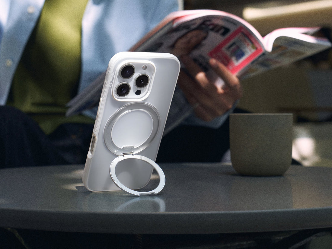 White phone case with a circular ring stand propped on a café table beside a cup
