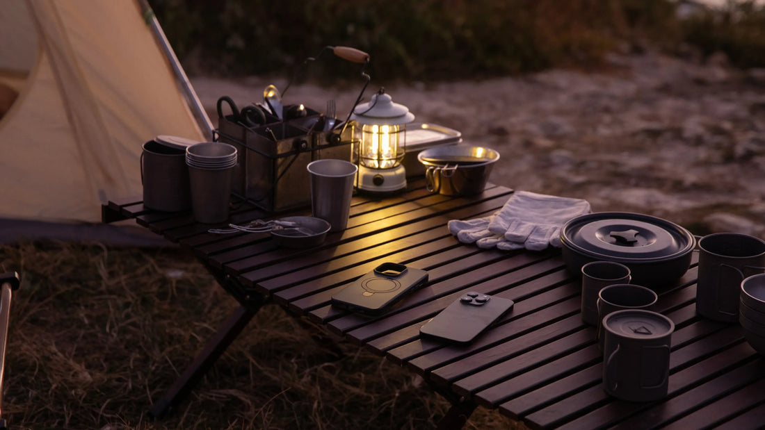 Outdoor table at dusk with lit lantern, camping cookware, and two smartphones arranged for stargazing.