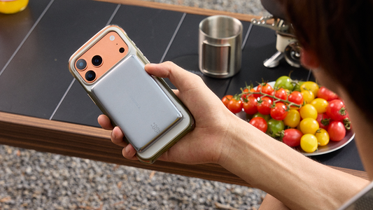 Hand holding an iPhone with a magnetic power bank near a plate of tomatoes