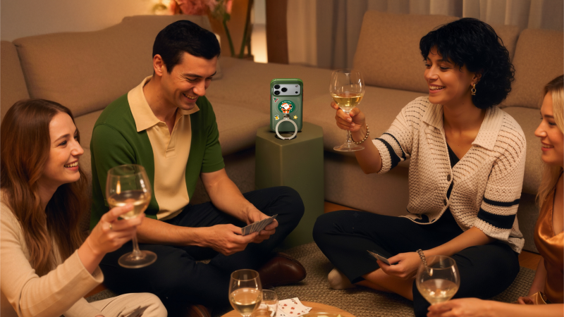Friends playing cards with a ring stand phone case propped in the room