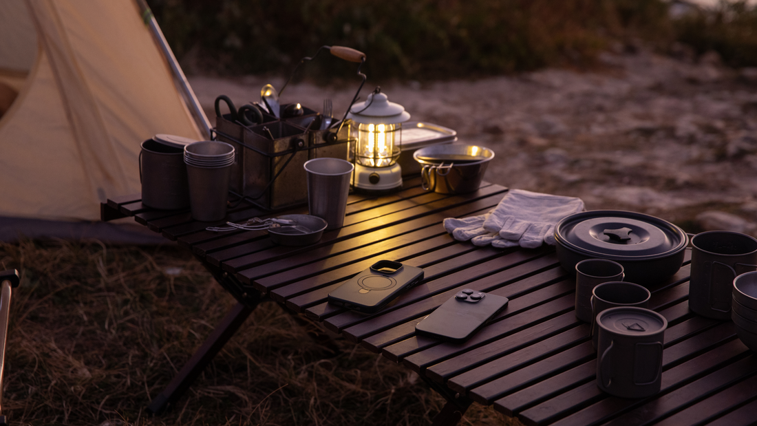 Camping table with cookware, lantern, and a MagSafe phone case beside a tent at dusk