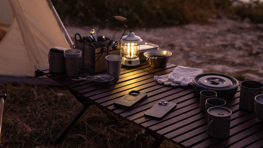 Camping table with cookware, lantern, and a MagSafe phone case beside a tent at dusk