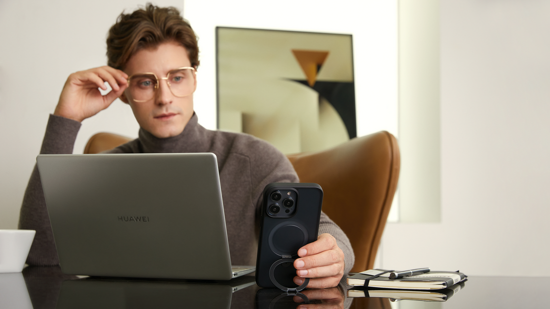 Man working at a laptop with a black MagSafe kickstand phone case on the desk