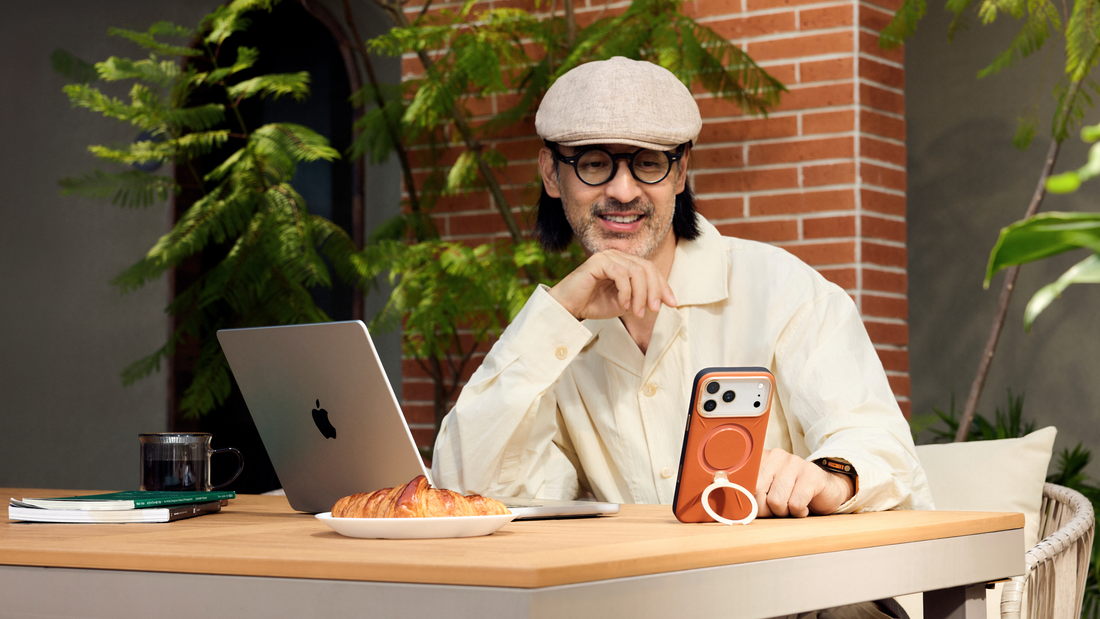 Man viewing a phone in an orange TORRAS case with a circular kickstand beside a laptop