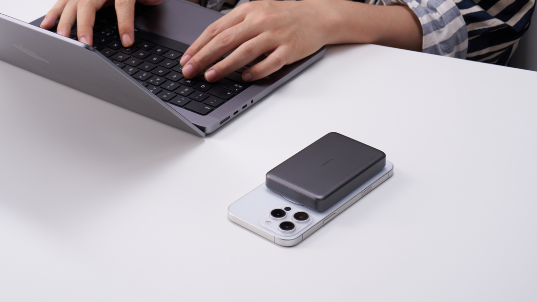 Dark gray TORRAS magnetic power bank attached to a white phone beside a laptop