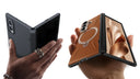 Hands holding black and brown foldable phones with protective hinge cases and magnetic rings