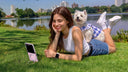 Woman relaxing with a small dog beside a pink foldable phone supported by its ring stand