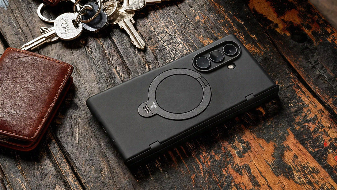 Black foldable phone in a magnetic ring case lying beside a wallet and keys on a wooden table