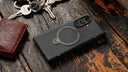 Black foldable phone in a magnetic ring case lying beside a wallet and keys on a wooden table
