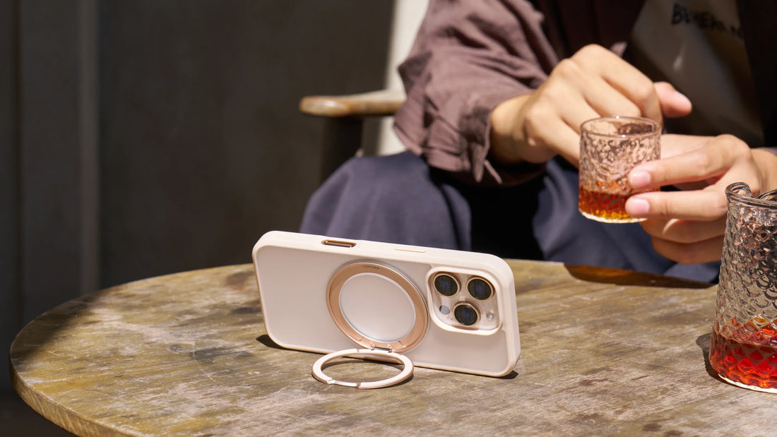 MagSafe phone case stand propped up on wooden café table while person holds iced tea