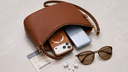Brown travel handbag with phone, power bank, earbuds, sunglasses, and boarding pass on marble surface