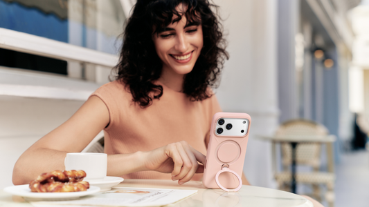 Woman at a cafe using a pink phone case with a built-in ring stand beside coffee and pastries
