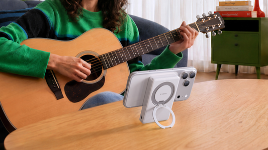 Person playing guitar beside a smartphone supported by a circular stand on a table