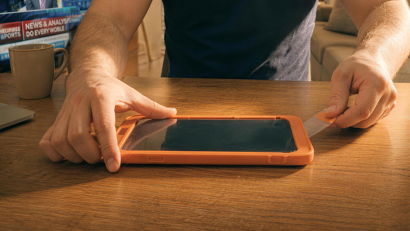 Hands applying a screen protector to a smartphone secured in an orange alignment tray