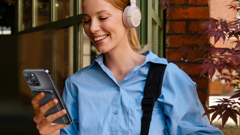 Woman wearing headphones and holding a smartphone with a card wallet attached