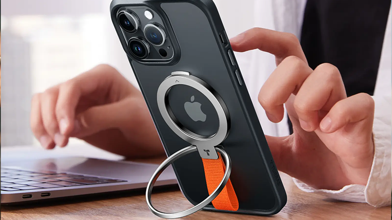 Smartphone supported by a metal ring stand beside a laptop on a wooden desk