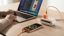 MacBook and iPhone charging on a desk with an orange cable and a compact charger