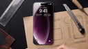 iPhone in a purple case lying on a designer desk with a craft knife, metal ruler and leather swatches