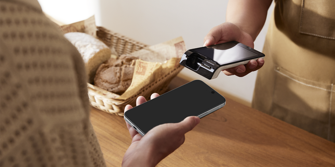 Person handing an iPhone to a customer at a bakery counter for a mobile payment