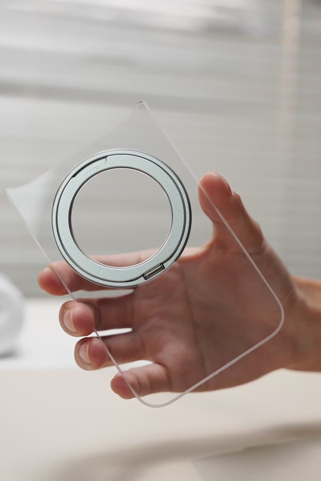 Hand holding a clear TORRAS case with a teal ring stand
