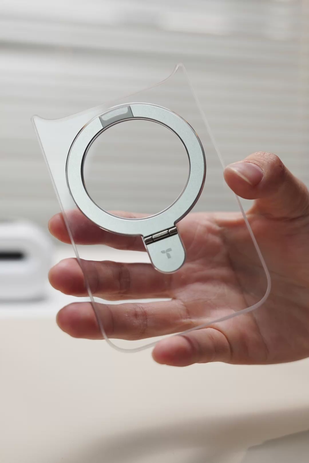 Hand holding a clear TORRAS case with a teal ring stand